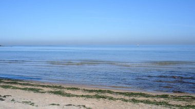 Kışın güneş ışığında açık mavi gökyüzü ve beyaz kumla deniz manzarası.