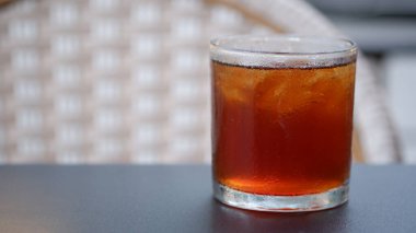 Siyah bir masada, arka planda rattan koltuğu olan buzlu çay..