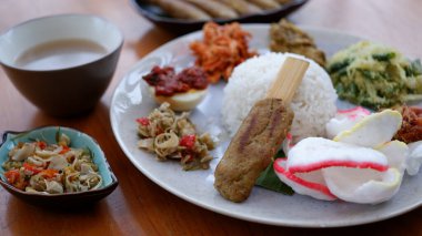 Beyaz bir tabakta Bali yemeğinden bir set. Haşlanmış pirinç, satay lilit, balado yumurtası, sambal, doğranmış tavuk, fıstık ve kraker..