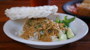 Beyaz tabakta beyaz krakerli Nasi Pecel. Fasulye filizli Nasi pekeli, biraz sebze ve ahşap masada fıstık sosu. Endonezya yemekleri.