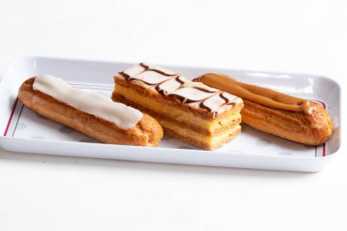 Patisseries millefeuille, eclairs a la vanille et au cafe dans un plat de presentation blanc