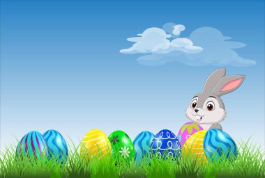 Paskalya yumurtaları bir tavşan ve arka planda mavi gökyüzü ile çimenlerin üzerinde dizilmiş.