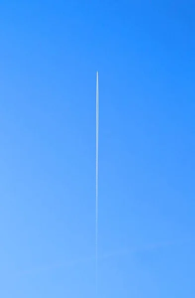 Airplane cloud line on a blue sky going straight up above, a flying jet speeding through the atmosphere and leaving a jet trail behind it in a straight line ascent