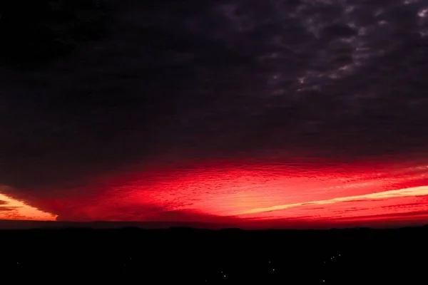 Яркий Красный Закат Вечером Задумчивыми Темными Облаками Городскими Огнями Внизу — стоковое фото
