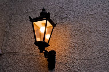 Narnia sokak lambası beyaz duvara sabitlenmiş. Öteki sokağı aydınlatıyor. Klasik, klasik, dekoratif bir retro dizayn lambasına yakın.