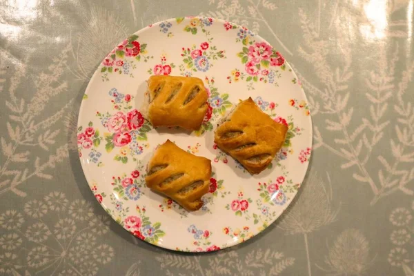 Cute mini sausage rolls on a plate on a table with floral table cloth, close up of freshly baked sausage roll to be eaten as fingerfood at a party or a delicious buffet appetizer finger-food close up