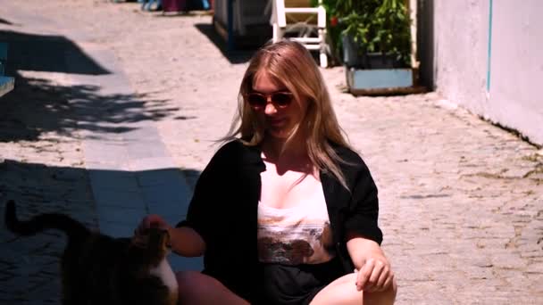身穿黑色泳衣 戴着太阳镜 头戴帽子的金发小女孩坐在街道岸边的码头上 — 图库视频影像