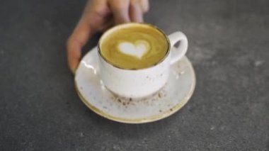 Erkek eli masadaki kapuçino bardağını verir, kahve üzerindeki kalp şeklini. Yüksek kaliteli FullHD görüntüler