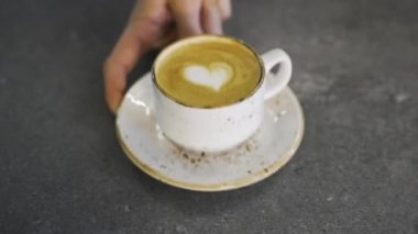 Erkek eli masadaki kapuçino bardağını verir, kahve üzerindeki kalp şeklini. Yüksek kaliteli FullHD görüntüler