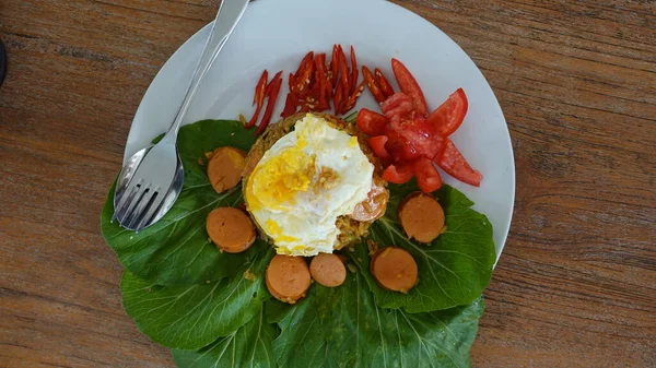 stock image close up of fried rice with egg and garnished with tomato, lettuce, sausage and mustard leaves on a white plate