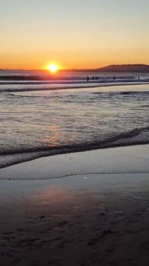 Almada yakınlarındaki Caparica 'da ve Portekiz' deki Lizbon 'da altın saat boyunca gün batımı çizgisinde. Akşamları plajda pembe yuvarlak güneş diski, insanlarla Atlantik Okyanusu 'nun dalgaları
