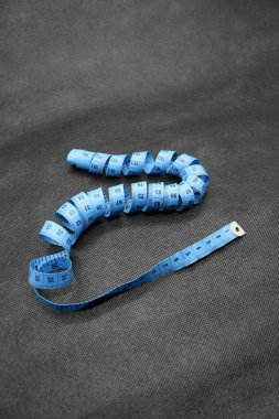 Bir kumaş ya da giysi ölçme aleti portresi, mavi ve siyah arka planı var. Ölçü Kaydı