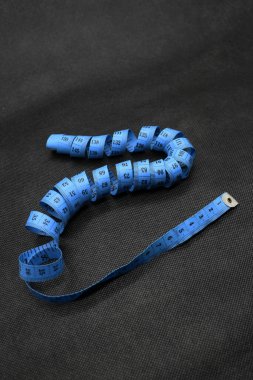 Bir kumaş ya da giysi ölçme aleti portresi, mavi ve siyah arka planı var. Ölçü Kaydı