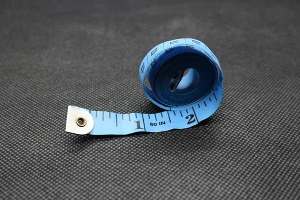 A portrait of a cloth or clothing measuring instrument, in blue with a black background. Measuring Tape