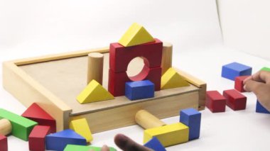 Beyaz arka planda toplanan renkli tahta yapboz oyuncakları oynayan bir çocuk