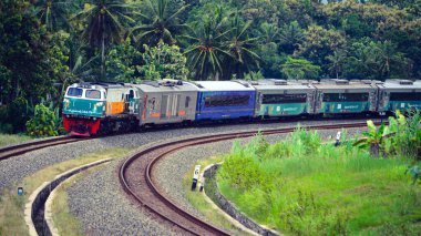 Kırsal ya da tepelik bir alanda hareket eden bir yolcu treni görüntüsü. İki tren hattı ve güzel manzarası var..