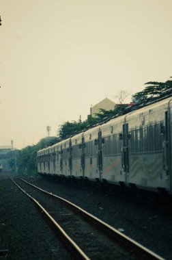 Kırsal ya da tepelik bir alanda hareket eden bir yolcu treni görüntüsü. İki tren hattı ve güzel manzarası var..