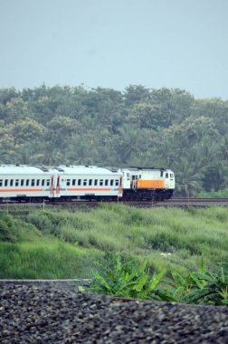 Kırsal ya da tepelik bir alanda hareket eden bir yolcu treni görüntüsü. İki tren hattı ve güzel manzarası var..