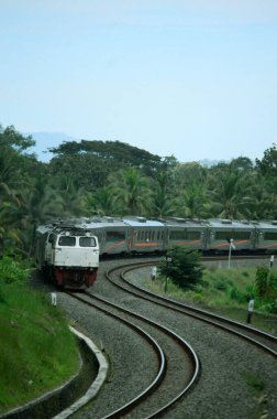 Kırsal ya da tepelik bir alanda hareket eden bir yolcu treni görüntüsü. İki tren hattı ve güzel manzarası var..