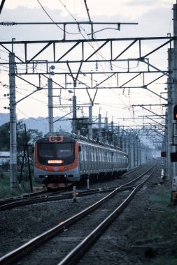 Kırsal ya da tepelik bir alanda hareket eden bir yolcu treni görüntüsü. İki tren hattı ve güzel manzarası var..
