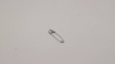 Emniyet iğnesi metalden ve gümüşten yapılmış, beyaz bir arka planı var..