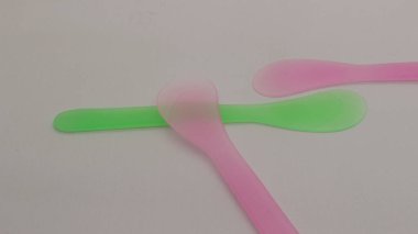 Pembe ve yeşil plastik maske spatulası beyaz arkaplanda izole edilmiş.