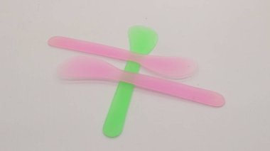 Pembe ve yeşil plastik maske spatulası beyaz arkaplanda izole edilmiş.
