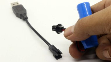 El ele tutuşan AA pil ve şarj kablosu beyaz arkaplanda izole edildi