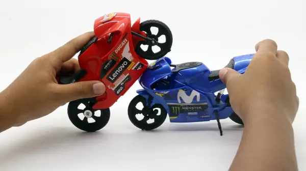 Çocuğun eli beyaz arka planda izole edilmiş küçük bir motosiklet oyuncağıyla oynuyor.
