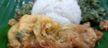 Muz yaprakları üzerinde servis edilen pirinç, yumurta, kalamar ve biber sosu menüsü..