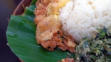 Muz yaprakları üzerinde servis edilen pirinç, yumurta, kalamar ve biber sosu menüsü..