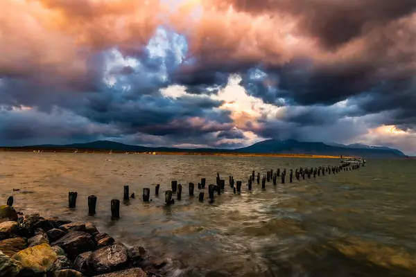 stock image Stunning view of the historic pier of Puerto Natales, Chile, on the Seoret Channel, at sunrise on a summer day with the sky covered in gray and pink clouds