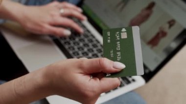 Bilgisayarlı e-bankacılık hizmetleri kullanan kadın kredi kartını elinde tutarak güvenli bir ödeme yapıyor. Kadın alıcı internet sitesine e-ticaret servisi aracılığıyla ödeme yapıyor. Evdeki kanepede oturuyor. Görüntüyü kapat
