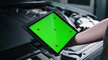 Tanımlanamayan erkek araba servisi çalışanı, açık kaputun yanında dururken yeşil ekran kromatonlu dijital tablet bilgisayar kullanarak arabayı kontrol ediyor ve bakım yapıyor.