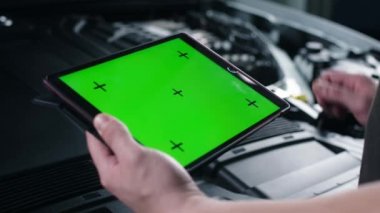 Unrecognizable male car service worker checking car and doing maintenance using a digital tablet computer with green screen chromakey, while standing near the opened bonnet