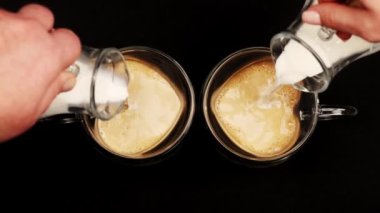Bir erkek ve bir kadın kalp şeklinde bardakta sütlü kahve yapmak için süt dökerler. Kafe atölyesi. Latte espresso ve buğulanmış kahveden yapılan bir içecektir. B-rulo. Sevgililer Günü