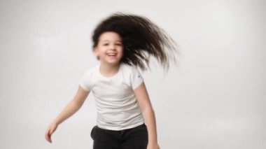 A little charming curly girl with a charming smile listens to music in wireless headphones and dances. Positive emotions of the child. Isolated, on a white background