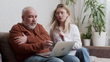 Smiling Daughter teaching her father how to make payment using online banking on a laptop. A beautiful and traditional young woman showing an elderly man how to shop buy things online.