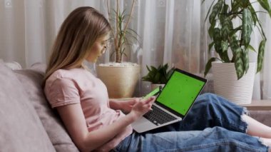 Bir kadın Chromakey dizüstü bilgisayarı olan yeşil bir akıllı telefon ekranı kullanıyor. Parmağını yeşil ekranda gezdirip dizüstü bilgisayarla çalışan bir kadının yakın plan fotoğrafı..