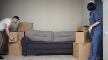 Joyful young married couple sitting on the sofa and smiling after unpacking and decorating their new apartment with many boxes. A European couple, wife and husband, are resting after moving in.