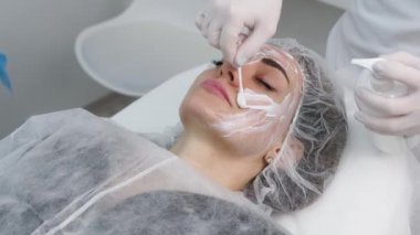 Cosmetologist is applying cream with anesthesia on patient's face skin before biorevitalization procedure. Woman in beauty clinic with doctor beautician preparing to treatment using numbing cream.