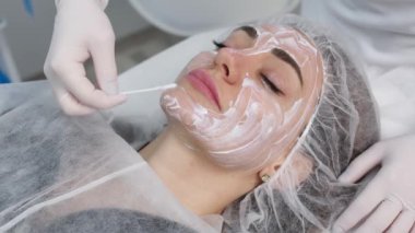 Cosmetologist is applying cream with anesthesia on patient's face skin before biorevitalization procedure. Woman in beauty clinic with doctor beautician preparing to treatment using numbing cream.