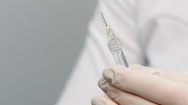 Close-up of syringe with drop (solid jelly-like soft material. hyaluronic acid filler). Preparing needle for injection on a light background.