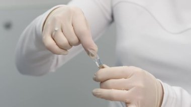 Close-up of syringe with drop (solid jelly-like soft material. hyaluronic acid filler). Preparing needle for injection on a light background.