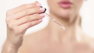 Genç bir kadınla yakın çekim stüdyo portresi, izole edilmiş, bir pipetten yağlı bir serum uyguluyor. Yüz bakımı ve cilt yenilenmesi için doğal organik kozmetik ürünler
