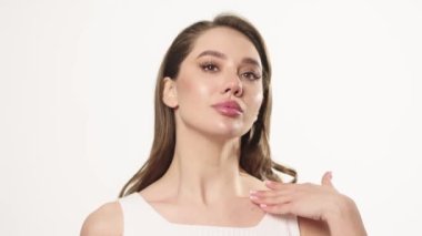 Portrait of a woman standing against a white background applying a nourishing body cream. Enjoy the process of smiling while taking care of perfect skin. Women's skin care after product advertising
