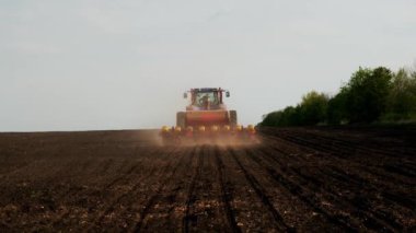 Farmer on tractor with seeding machinery driving over field sows grain of wheat or corn. Concept of work in agronomic farm for making business and having profit from production organic food