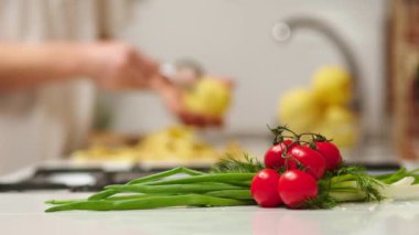 Close up view of woman in white shirt peeling a potato. Peel falling onto cutting board. Lady preparing potatoes to be cut and added to stock pot for dinner.