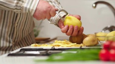 Bachelor man preparing dinner at home in the kitchen. Healthy food theme, male peels the skin on raw potatoes close-up over the table. Non-GMO vegetables from the farm. Man's hands peeling potatoes.