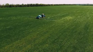 Spraying a green wheat field by tractor. The farming tractor spraying on field with sprayer, herbicides and pesticides. Industrial machine fertilizing a field. Chemicals used by agricultural tractor.